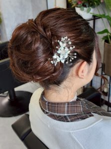 細かい編み込みを入れたシニヨンに、かすみ草風の白いヘアアクセをあしらったブラウンヘアのアップスタイル