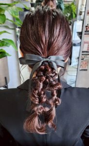 黒いリボンで結んだローポニーから立体的な編み込みを連ねた、ロングヘアのガーリーなルーズ二股編みおろしヘア
