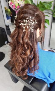 細かな編み込みと小さな白い花飾りをあしらった、ロングカールの華やかなハーフアップスタイル