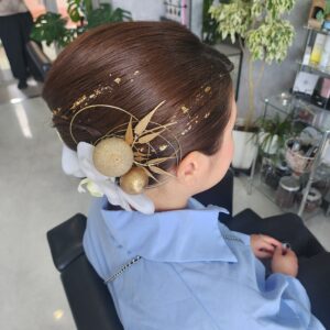 成人式や結婚式にぴったりの華やかな和装ヘアアレンジ。金箔ヘアとゴールドの水引、大輪の白い花を組み合わせた、面を活かした上品なアップスタイル。