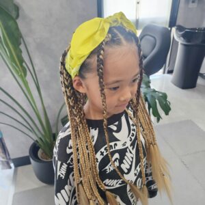 美容室で施術されたキッズの特殊ヘアセット。黒とブロンドのエクステンションを編み込んだロングブレイズに、黄色いバンダナを合わせた後ろ姿。