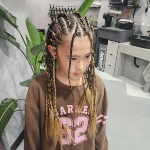 ​キッズ特殊ヘアのコーンロウとブレイズのミックススタイル。黒とゴールド（ブロンド）のエクステンションを使用し、正確なブロック分割で編み込まれている。ダンス発表会やイベント、B系ファッションにおすすめ。