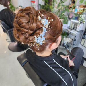 立体的な毛流れが美しいルーズなアップヘア。暖色系カラーに映える青い花飾りを添えた、プロによる高度なヘアセット技術。