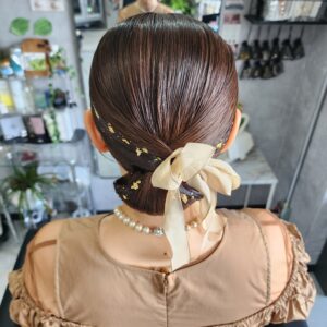 面の艶を最大限に活かした、タイトなシニヨンアレンジ。トレンドの金箔ヘアに、柔らかなベージュのリボンをプラスして和洋折衷な雰囲気に。結婚式のお呼ばれやセレモニーにふさわしい、崩れにくく品格のあるアップスタイルです