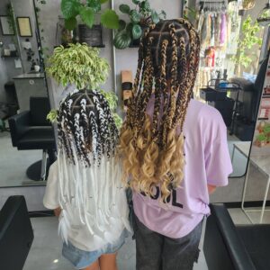 美容室で施術された、キッズの特殊ヘアセット事例。白と黒のモノトーンブレイズに白い羽のような毛先（左）と、黒とブロンドのハーフカラーにカールの毛先（右）をした2人の女の子の後ろ姿。