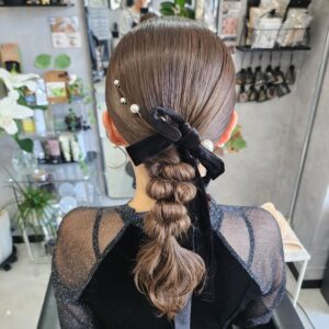 表面タイトに面を出して下めにローポニーにし、ポコポコとしたたまねぎヘアに編みおろされたスタイル。パールとベルベットのリボンをアクセントに飾りつけられている。
